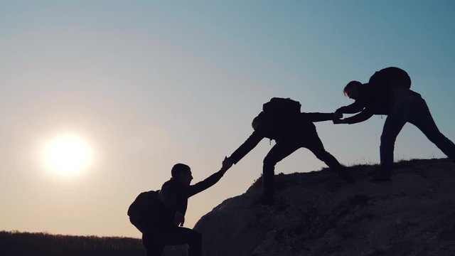 At sunset, tourists climb the mountain, overcoming obstacles. Silhouettes of men helping each other in a difficult situation. A friend, a young man, gives a helping hand.