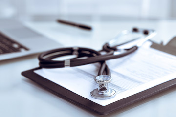 Stethoscope lying at the desk with medical history records and laptop computer. Medicine doctor's working table concept