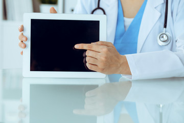 Female doctor using tablet computer while sitting at the workplace, close-up of hands. Medicine, healthcare and help concept