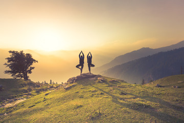 Two men perform Yoga (vrikshasana - Tree pose) on a mountain at Deo Tibba trek in Manali, Himachal...