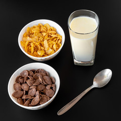 Blowl of corn and choco flakes with glasss of milk and spoon on black gray isolated background.  a delicious and healthy dietary breakfast cereal. Top View