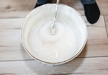 Man is mixing spackling glue in the bucket. Wallpaper hanging in the flat. Restoration indoors. Renovation works.