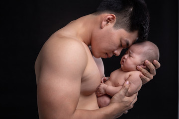 The baby sleeps in the hands of a strong father.