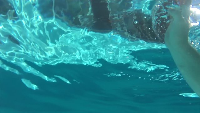 A hand underwater touching the surface of the pool.