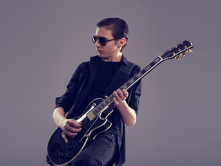 Fifteen years old guitarist with a  black electric guitar. Teenage musician holds guitar