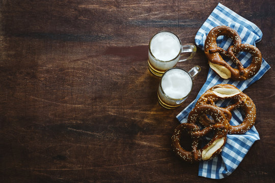 Sesame Pretzels And Beer Glasses On Dark Brown Wooden Table. Traditional German Appetizer. Oktoberfest Background