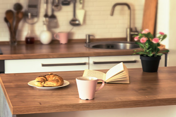 Coffee latte, book and croissant on wooden table. Modern kitchen interior background. Shallow depth of field