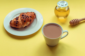 Breakfast, morning coffee with milk, croissant and honey on yellow background, top view, close up.