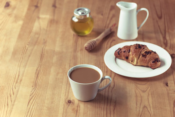 Breakfast: morning coffee, croissant, honey and milk on wooden table, top view. Copy space.