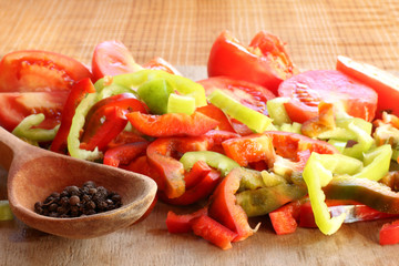 seasoning spoon and slices of fresh pepper with tomatoes on a cutting board front view. cooking veggie salad from vegetables