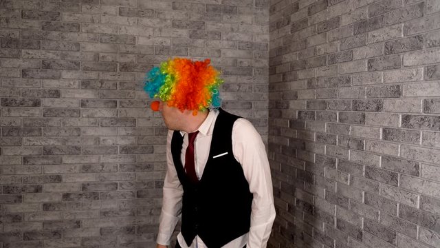 A man picks his nose at work. Office worker in clown wig, clown concept at work. Businessman with clown wig. Original clown costume for Halloween