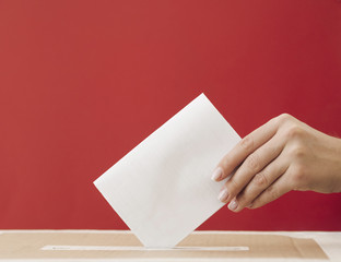 Side view woman putting a ballot in a box with red background