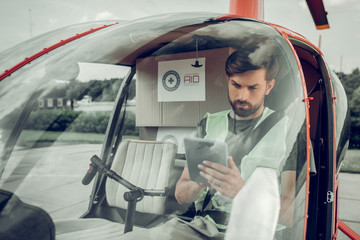 Bearded pilot using his tablet while sitting in little helicopter