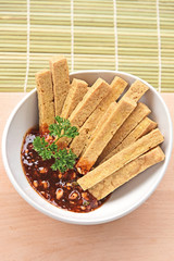 Fried Tofu with Dipping sauce in white bowl on bamboo mat. vegetarian menu.