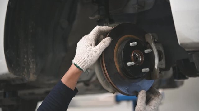 Asian male mechanical hold and shining flashlight to examine car disk brake pad wear of automotive vehicle. Safety suspension inspection check service maintenance for customer before road trip. 4K