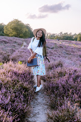 young girl with dress and hat visiting the blooming Heather field Posbank Veluwezoom in the Netherlands, purpple hills with blooming flowers