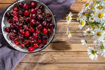 Concept cherry harvest and bouquet of wildflowers as a rustic simple still life. Flatlay whith copy spase.