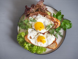 Fried bread sandwich with scrambled eggs and fresh salad leaves for Breakfast on a plate, top view