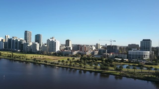 Beautiful scenic aerial view of drone flight above Swan River along the skyline of Perth, capital of Western Australia, with summer sunny blue sky and horizon as background.