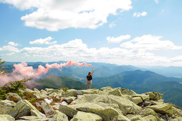 Beautiful woman with red colored smoke at the top of the mountain and cloudy sky background