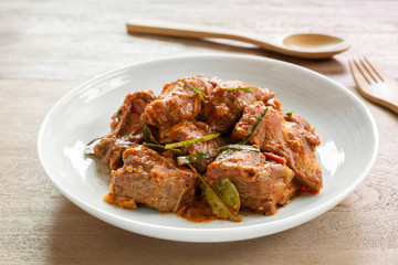 close up of stir fried pork rib with red curry paste in a ceramic dish on wooden table. hot and spicy thai style food menu.