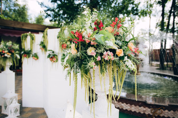 beautiful wedding photo zone in the park with fountains in the shade, a white screen, a pedestal with flowers and decor. Wedding screen