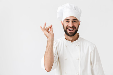 Cheerful pleased young chef posing isolated over white wall background in uniform.