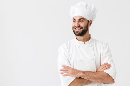 Pleased happy young chef posing isolated over white wall background in uniform.