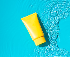 Sun cream yellow tube on the blue water surface. Summer vacation  cosmetics concept. Top view