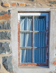 An old wood framed window with a striped curtain isolated in a rock wall image with copy space in vertical format