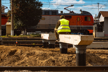 Railroad worker sits on the basis of a future passenger platform on the background of railways and wagons