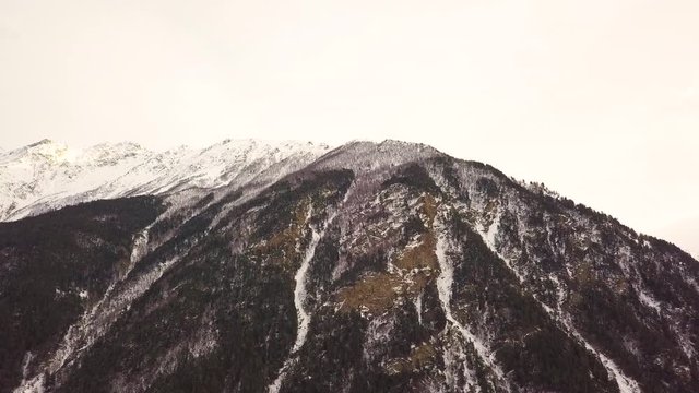 snow-capped mountain in cloudy weather, there are a lot of trees on the mountain aerial