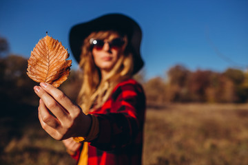 blonde woman holds a yellow leaf in the hands of the forest. Autumn forest. sunny autumn weather. Girl in a red jacket in the autumn forest.