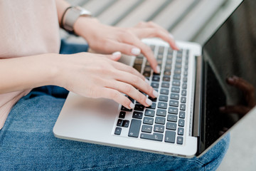 female hands typing on laptop keyboard outdoors