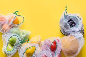 Frame of reusable mesh bags with fruits and vegetables on yellow. Zero waste shopping. Ecological concept.