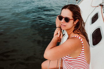 Pretty young woman with striped sailor swimsuit enjoying a relaxing morning on a sailboat. Travel photography. Lifestyle