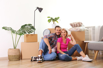 Young married couple moving in new apartment, sitting on the floor between many boxes. New home concept. Bearded man and blonde woman resting after a move-in. Background, copy space, close up.