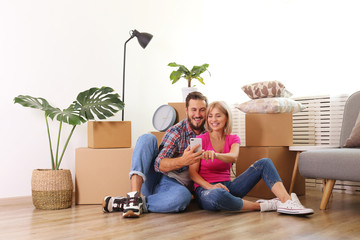 Young married couple moving in new apartment, sitting on the floor between many boxes. New home concept. Bearded man and blonde woman resting after a move-in. Background, copy space, close up.