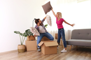 Young happy married couple having a pillow fight while taking a break from moving in into a new apartment. Many cardboard boxes on floor. Background, copy space close up.
