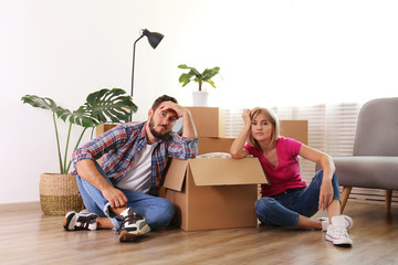 Young married couple moving in new apartment, sitting on the floor between many boxes. New home concept. Bearded man and blonde woman resting after a move-in. Background, copy space, close up.