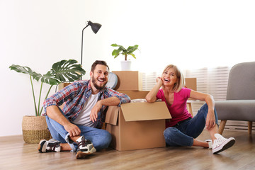 Young married couple moving in new apartment, sitting on the floor between many boxes. New home concept. Bearded man and blonde woman resting after a move-in. Background, copy space, close up.