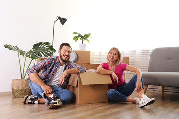 Young married couple moving in new apartment, sitting on the floor between many boxes. New home concept. Bearded man and blonde woman resting after a move-in. Background, copy space, close up.