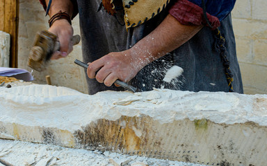Stonemason With Ancient Costume During The Processing Of The Stone With Chisel. In evidence a fragment of stone that squirts