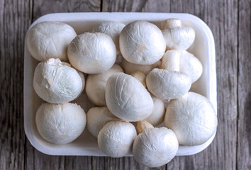 champignon mushrooms in a white container on a wooden background close-up