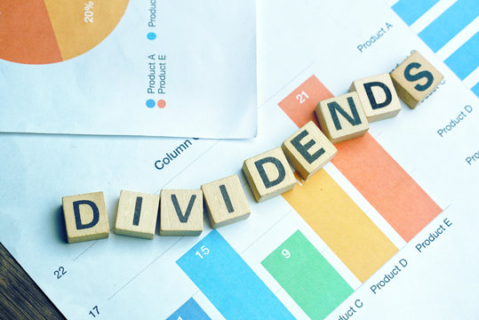 Text "DIVIDENDS" on wood dice which lay on graph volume document for up trend in stock investment concept.