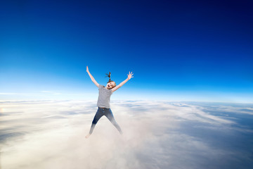 Fototapeta premium Little girl flying over clouds in the blue sky.