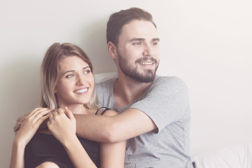 Couple in bed. Young white male and blonde female. Sitting in bed with happy smile. Modern couple lifestyle concept. With light leak.