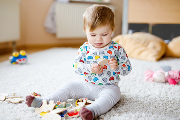Gorgeous cute beautiful little baby girl playing with educational toys like wooden puzzle at home or nursery. Happy healthy child having fun with colorful different toys. Kid learning different skills