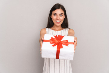 Image of happy brunette woman wearing dress smiling and holding present box at camera