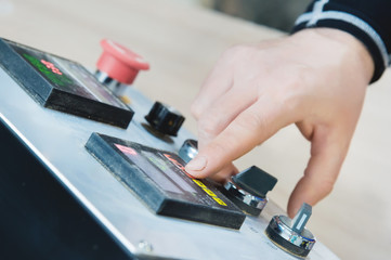 Close-up of a male hand on a dashboard controlling production equipment with buttons and displays in a locksmith's workshop for furniture production